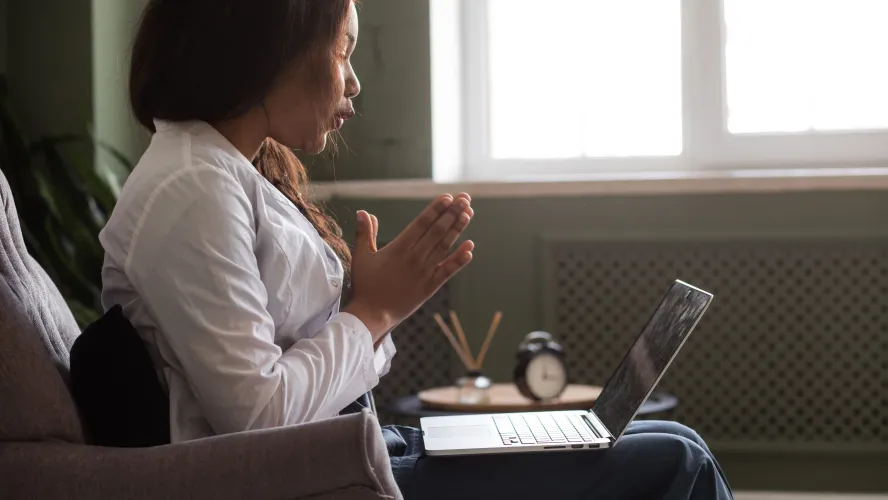 Woman in white coat communicating virtually on laptop
