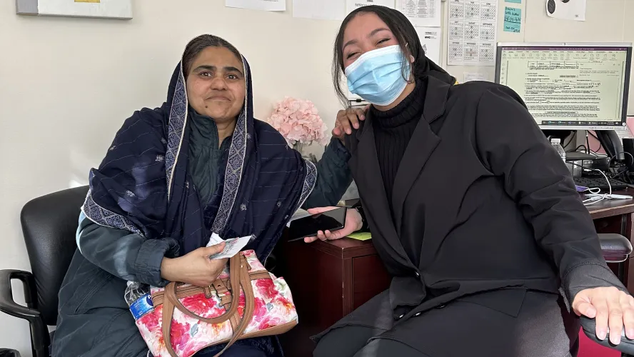 Two women sitting in office, one wearing face mask