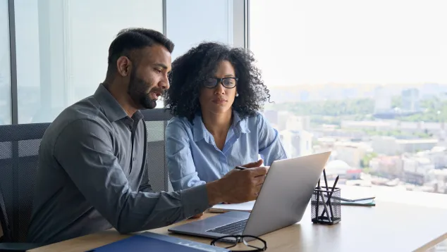 Two colleagues discussing work using laptop in office