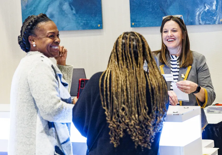 Three women engaged in conversation at registration desk