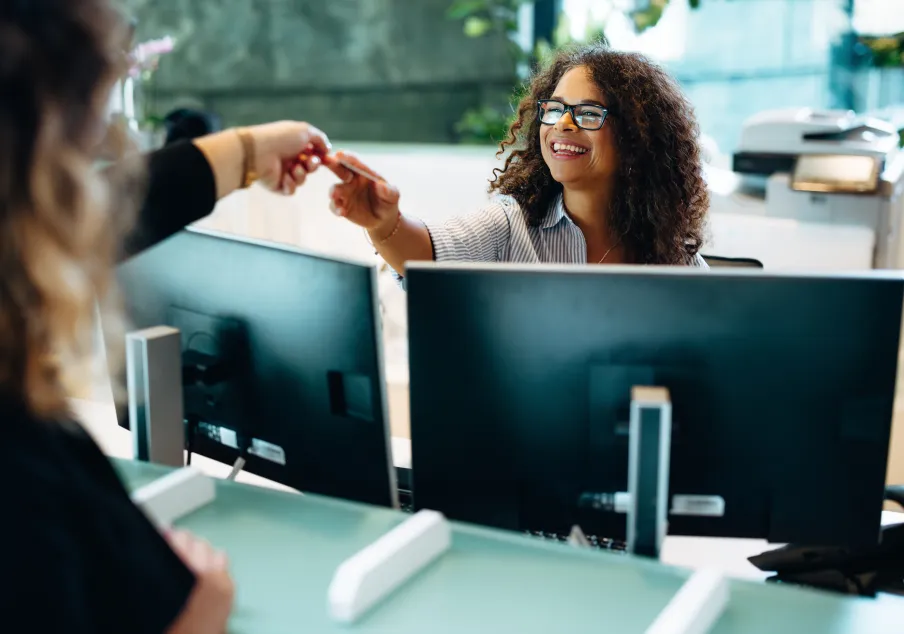 Receptionist smiling while handing card to visitor at desk