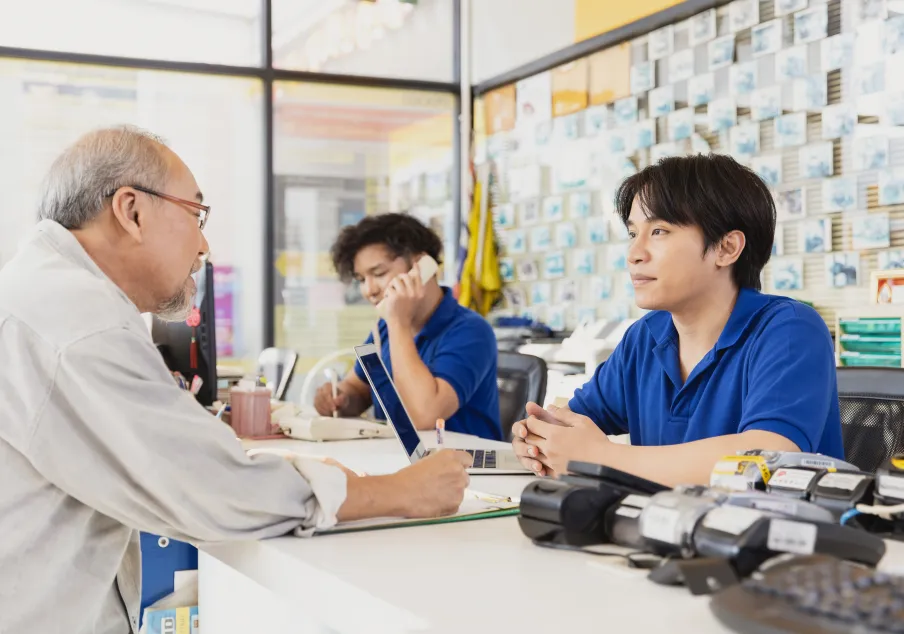 Customer service representatives assisting elderly man at office desk