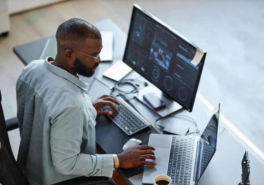 A man at a desk looking at data on two computers