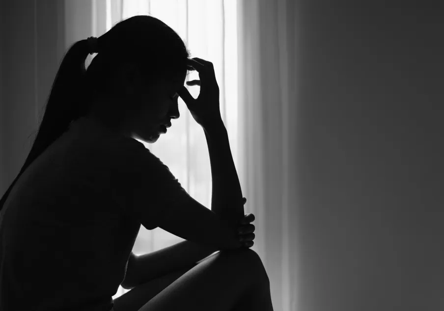 Woman sitting in silhouette with hand on forehead, contemplative.