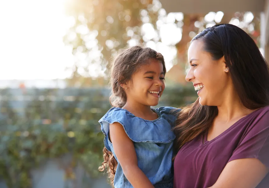 Smiling woman holding laughing young girl outdoors together