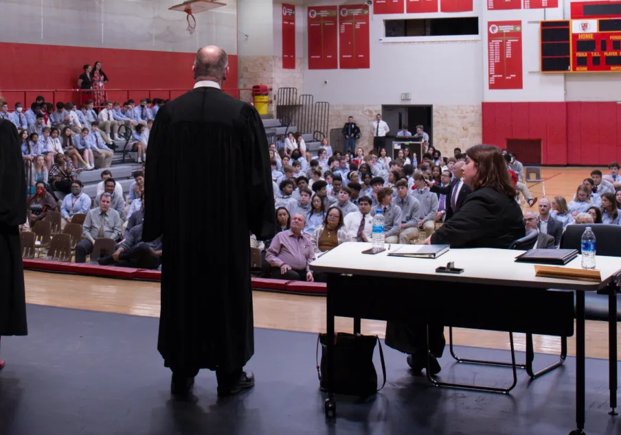 Judges speaking to students in school gymnasium assembly.