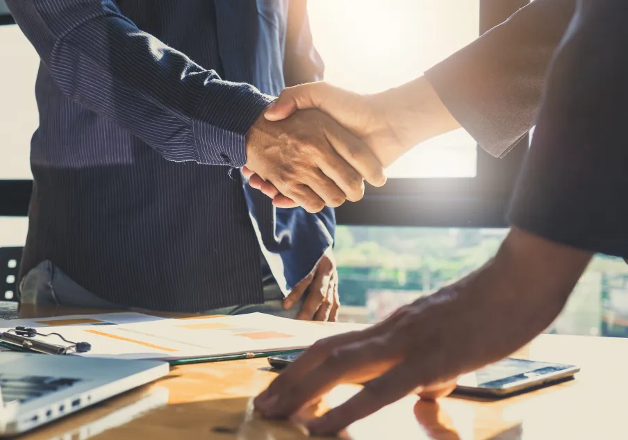 Two people shaking hands over desk with documents