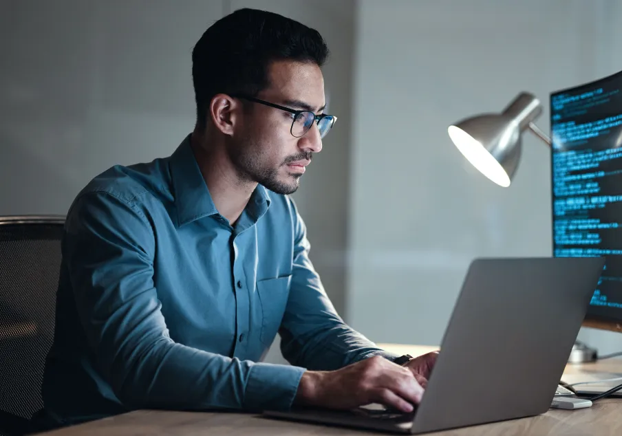 Man in glasses working on laptop with coding on monitor