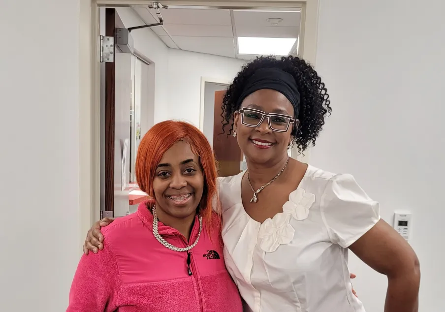 Two women standing together smiling in office hallway