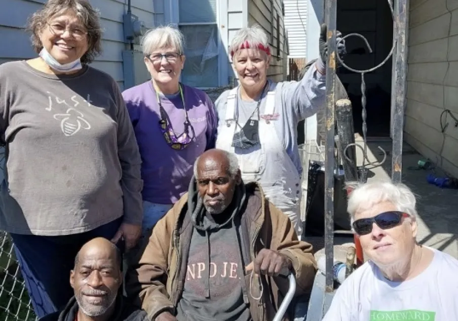 Diverse group of adults posing outside residential buildings.