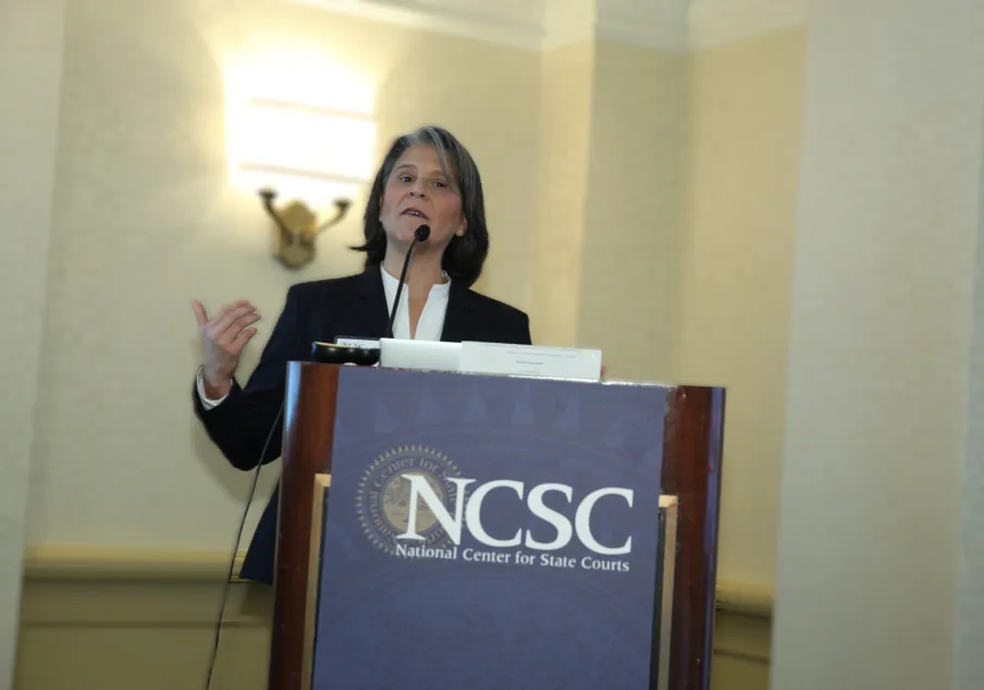 Woman speaking at podium with NCSC banner visible