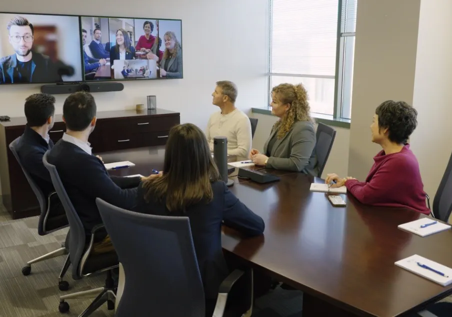 Conference room video call with diverse professionals and technology.