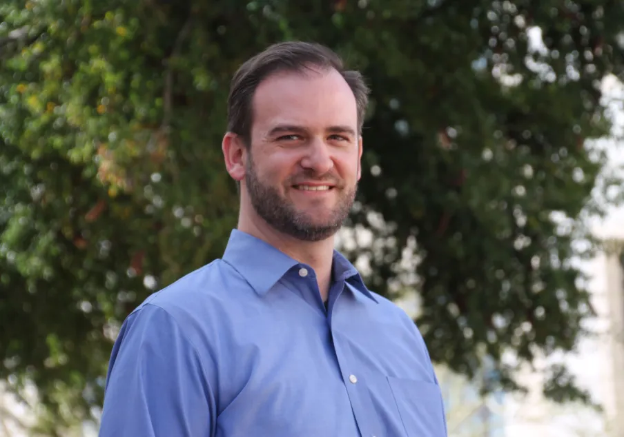 Man in blue collared shirt outdoor with trees background