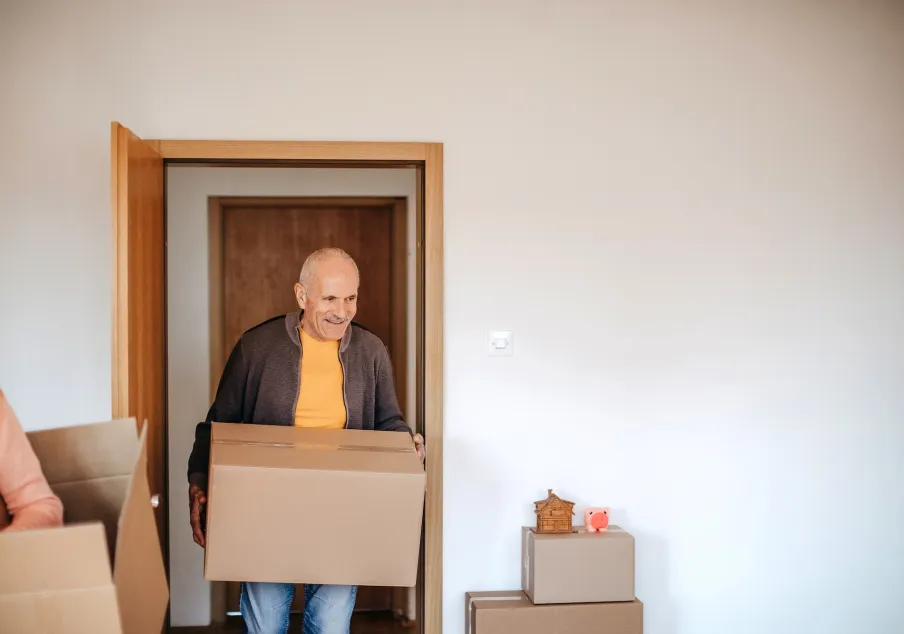 Smiling older man carrying moving box into empty home