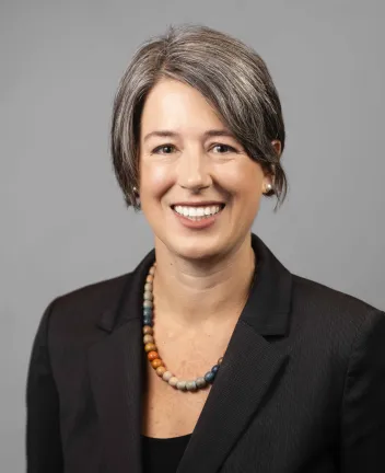 Professional woman in black blazer smiling against gray background