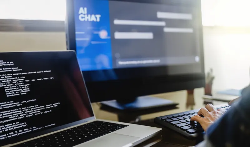 Person typing on keyboard with laptops showing AI chat interface