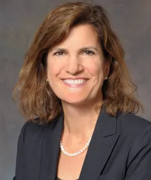 Professional woman with pearl necklace smiling, gray background